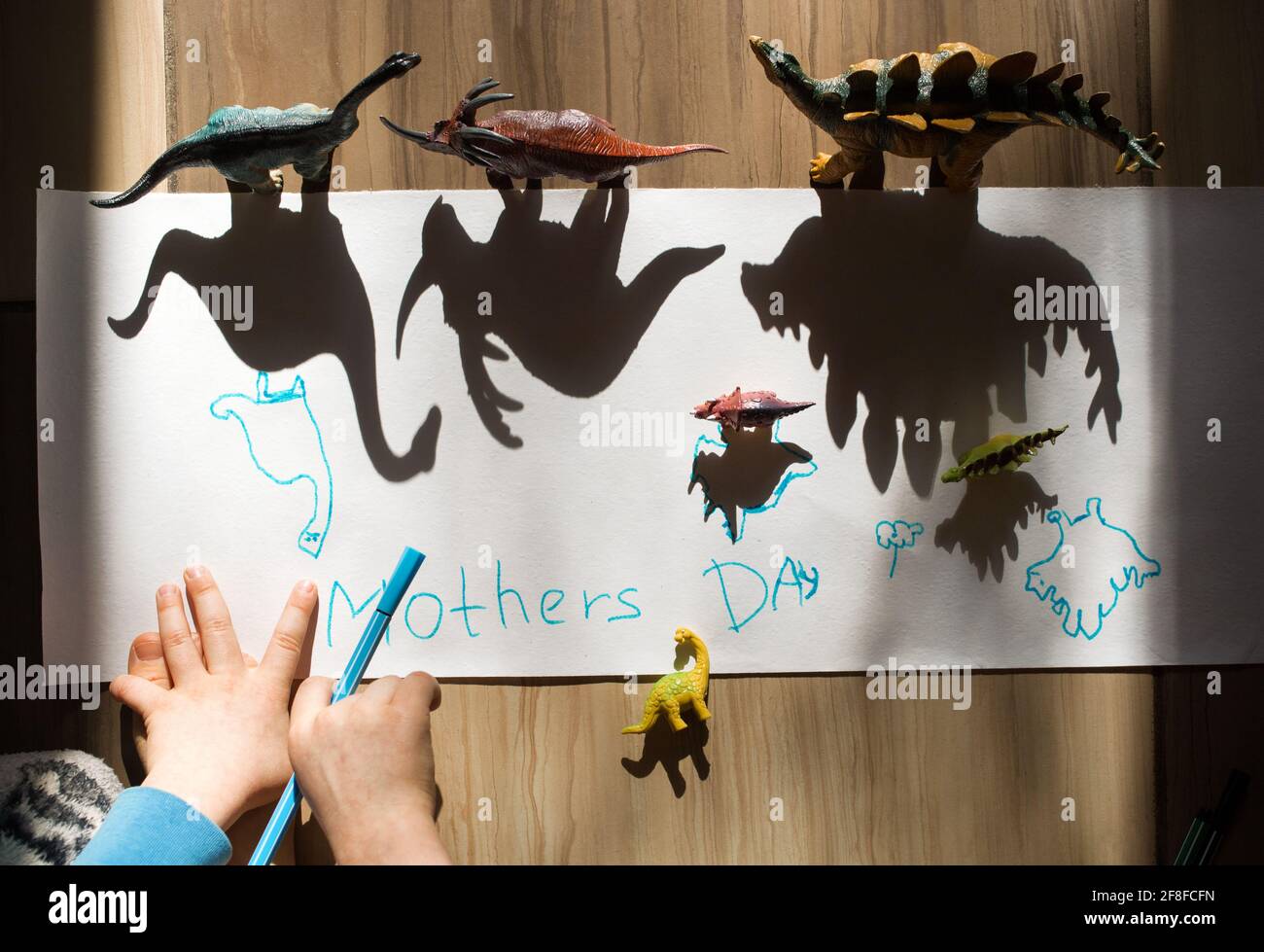 child is preparing a gift for mom for mother's day. outlines shadows of large and small dinosaur toy figures. ideas for creativity, development of fin Stock Photo