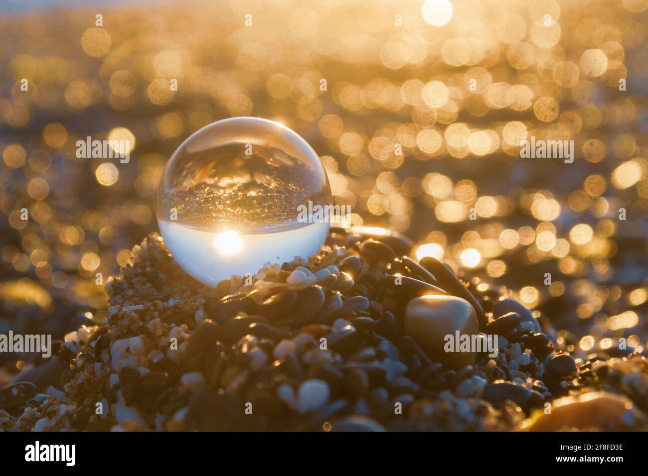 Glass round ball on the beach reflects the sea in summer at sunset ...
