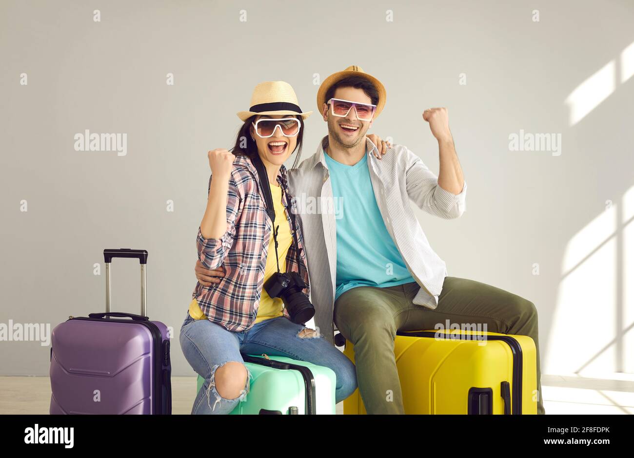 Joyful couple travelers in summer hat with photo camera, suitcase gesturing yes Stock Photo