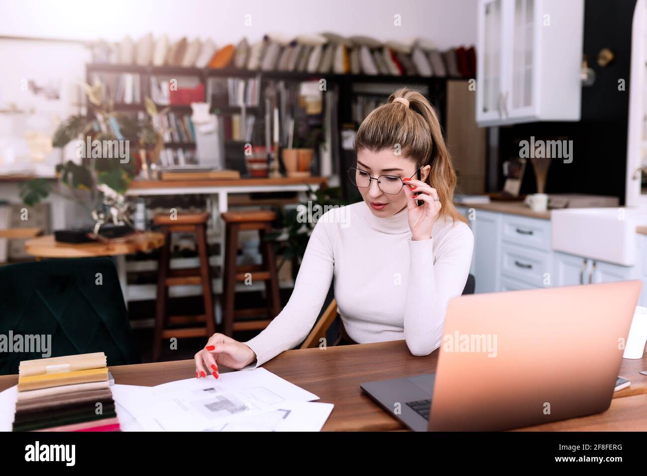 An interior designer is working on a new project, woman holding paper plan with pen. Considering the decision. Laptop on the desk. Thinking about new Stock Photo