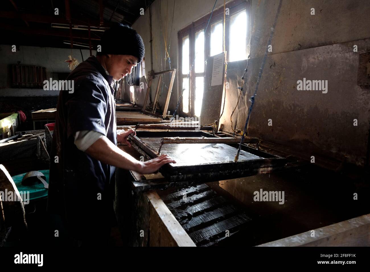 A worker prepares handmade paper at the Jungshi paper factory which uses traditional methods to produce the authentic Bhutanese paper known as Deh-sho from the bark of two tree species, the Daphne tree and Dhekap tree in Thimphu the capital of Bhutan. Deh-sho paper was originally used by monasteries for woodblock and manuscript books and also for writing prayer books. Stock Photo