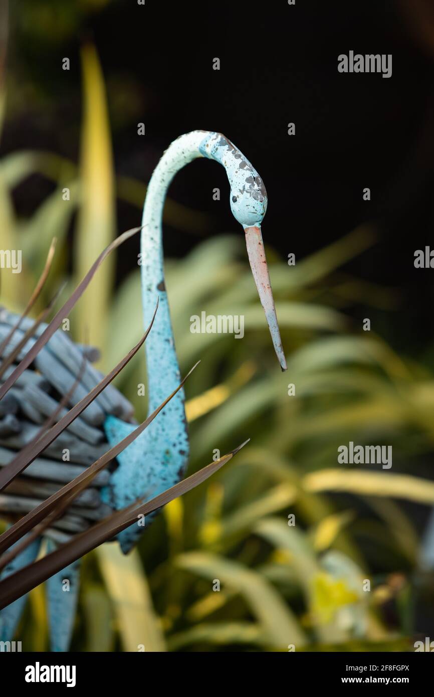 blue painted ornamental heron with wooden feathers in garden with fan shaped cordyline australis 'Red Star'' Stock Photo
