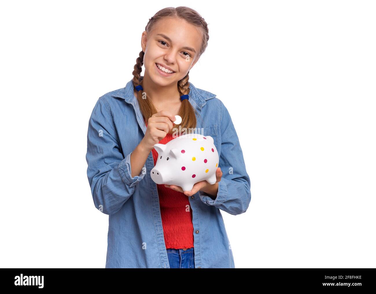 Beautiful teenage girl holds a piggy bank and a coin in her hands ...