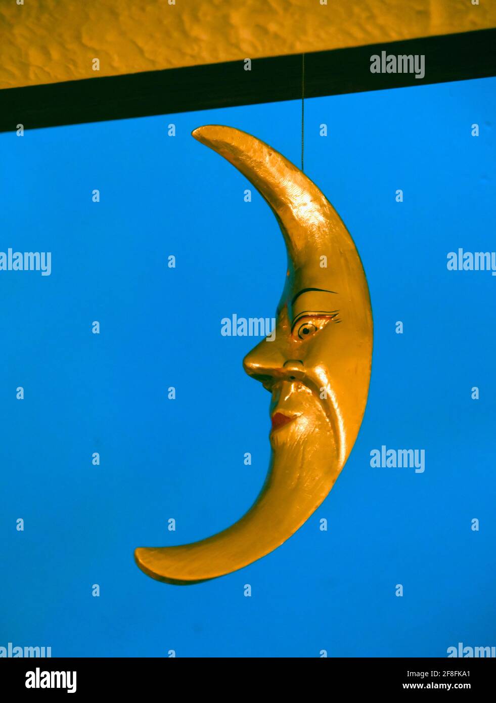 The Man in the Moon. Domestic ornament, gold coloured wooden crecent moon with eyes, nose and mouth. Stock Photo