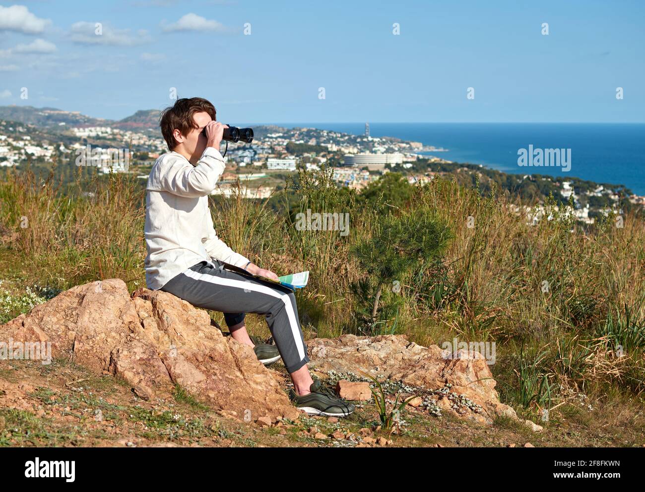 Adventurous young Spanish male traveler sitting on a rock using
