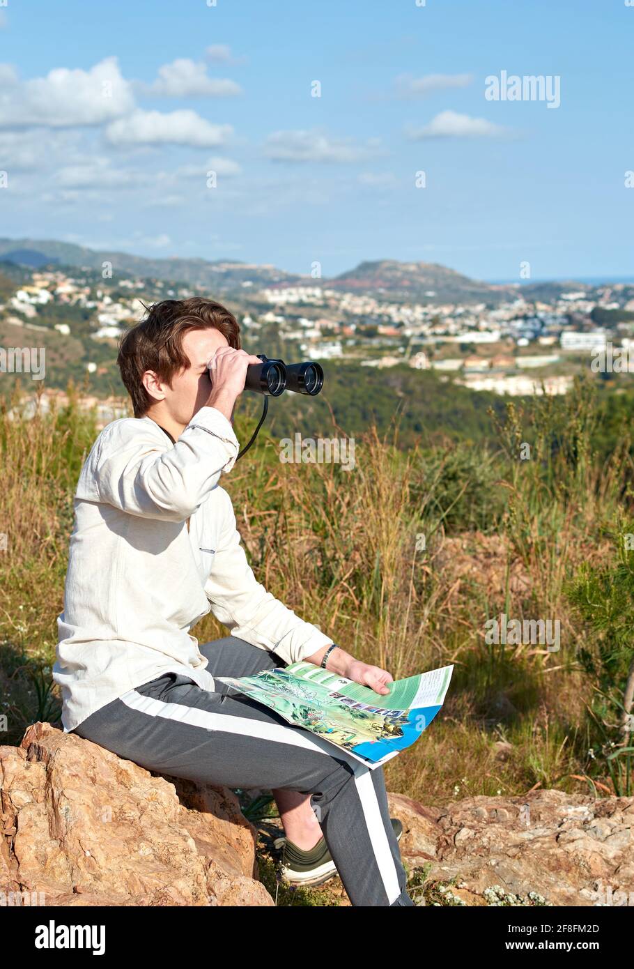 Adventurous young Spanish male traveler sitting on a rock using