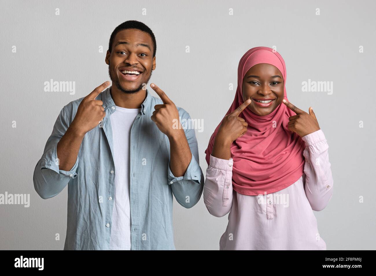 Smiling black man and woman pointing at their white teeth Stock Photo