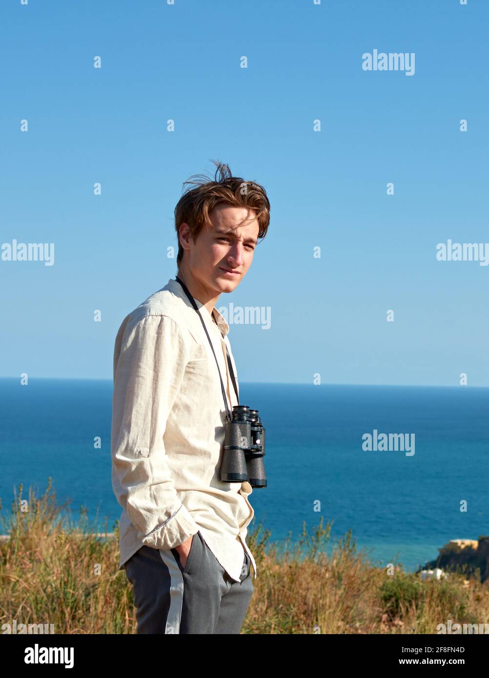 Portrait of a man with binoculars hanging around his neck posing for the camera in front of a sea Stock Photo