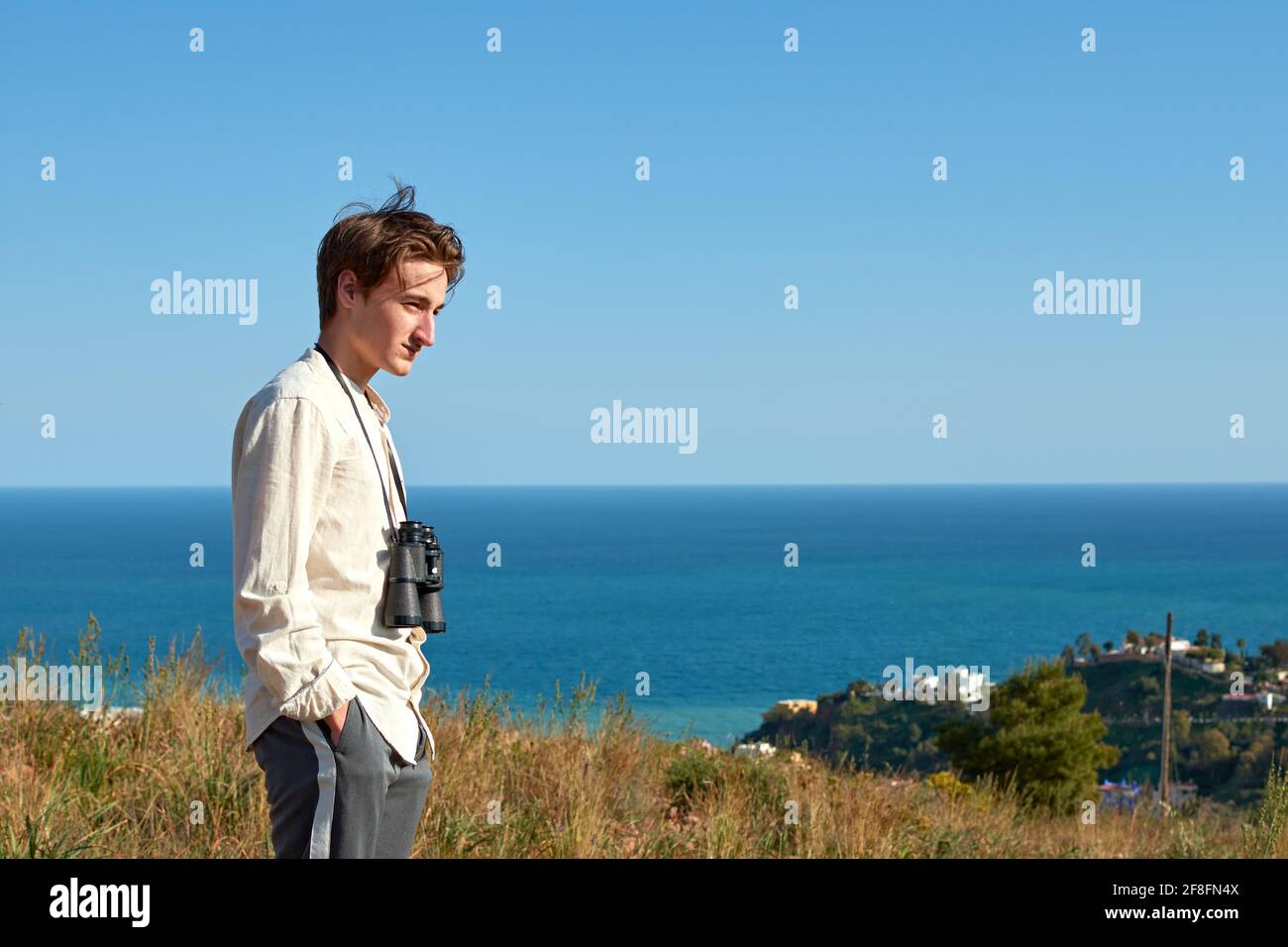Side view of a man with binoculars hanging around his neck posing for the camera in front of a sea Stock Photo