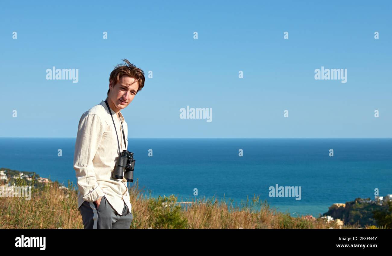 Portrait of a man with binoculars hanging around his neck posing for the camera in front of a sea Stock Photo