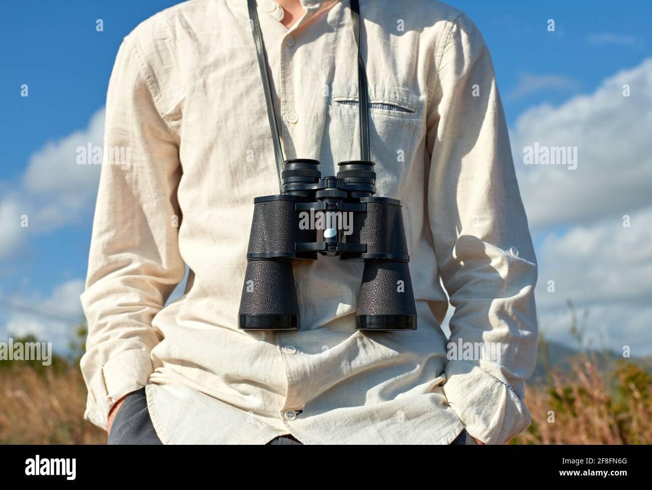 Closeup, front view of a relaxed young man in a white shirt with binoculars hanging around his neck Stock Photo