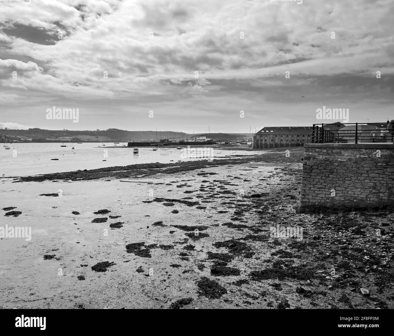 Tides Out. The riverside at Torpoint in south east Cornwall, with boats berthed on the harbour wall. In the distance Mount Edgcumbe. Black and White i Stock Photo