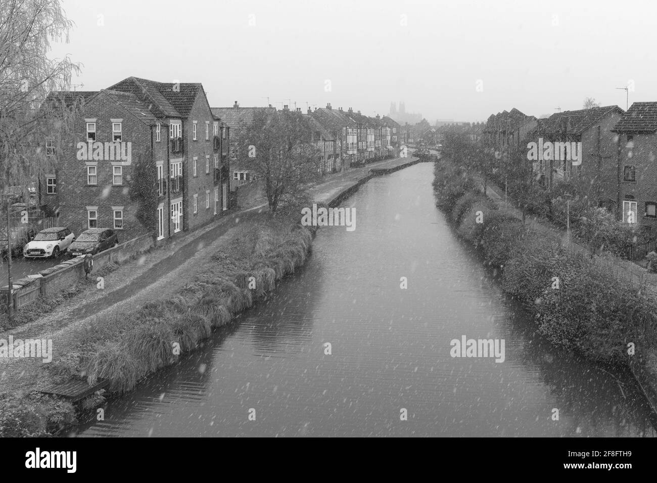 Snow falls in spring over the beck flanked by town houses on a bleak morning in Beverley, Yorkshire, UK. Stock Photo