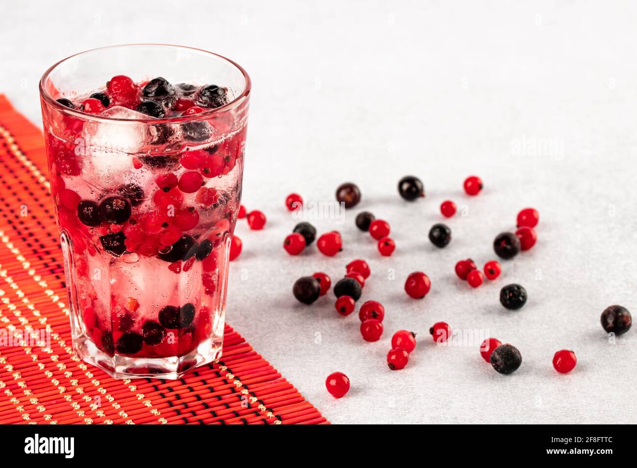 Summer cold drink with water, ice and multicolor berries. A glass of red and black currants on a gray background. Fruitarianism, veganism concept. Veg Stock Photo