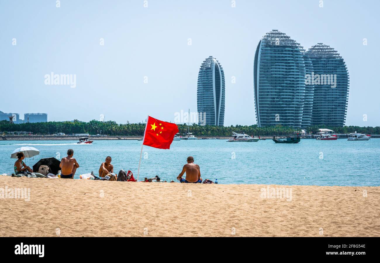 Sanya China , 24 March 2021 : Group of people around a Chinese flag on Sanya beach and view of buildings of Phoenix island in the bay in Sanya Hainan Stock Photo