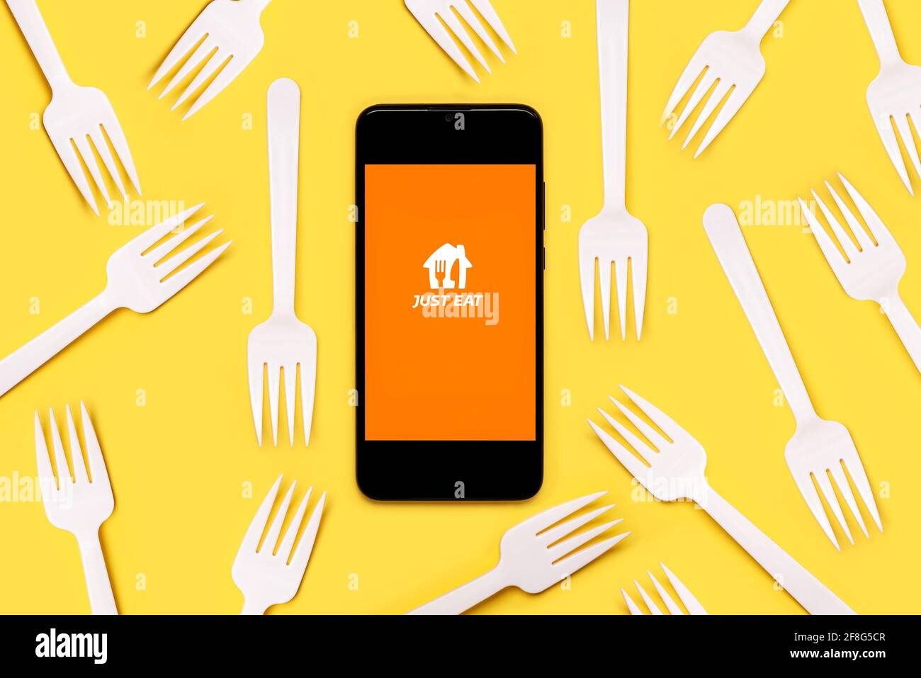 Just eat application icon on black screen of smartphone with white plastic forks on yellow background Stock Photo