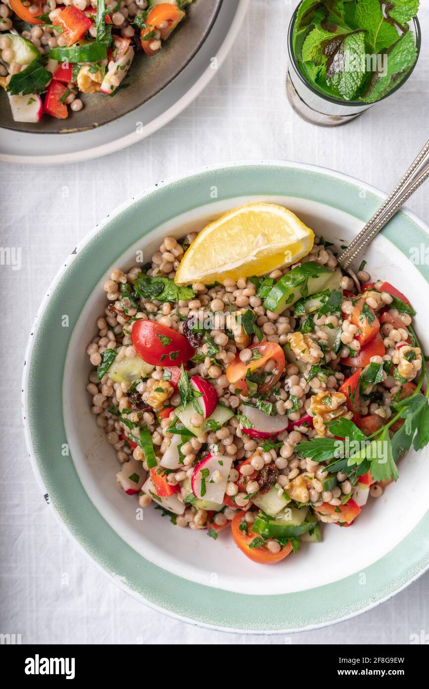Flatlay of two bowls with healthy vegan wholewheat pearl couscous salad with lemon ad fresh vegetables on a white background, with copy space Stock Photo
