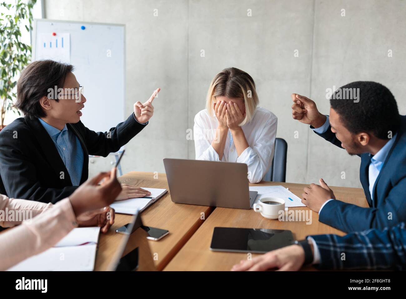 Colleagues Shouting At Unhappy Victimized Businesswoman Sitting In Modern Office Stock Photo