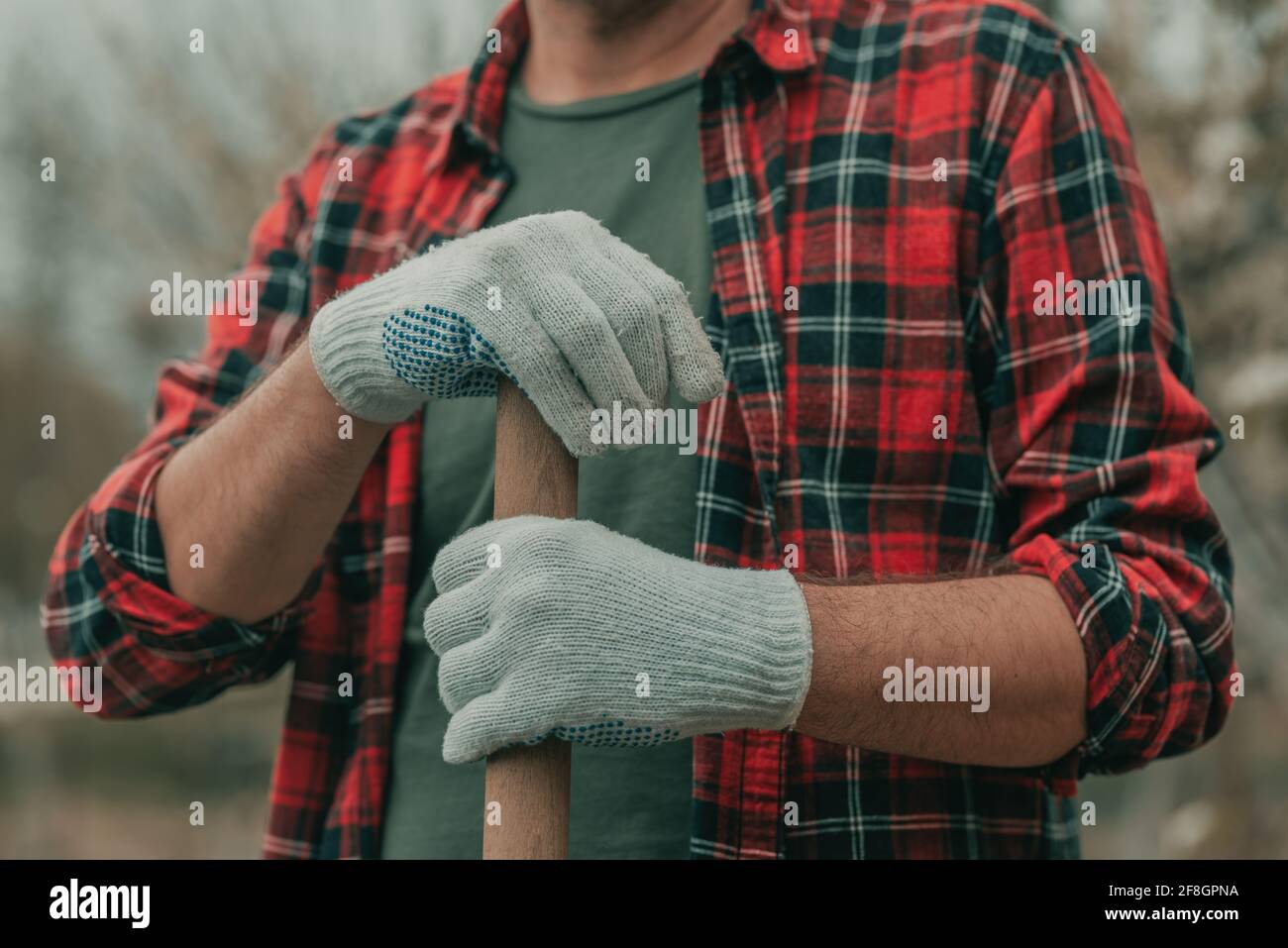 Farmer holding a spade shaft, resting in the garden during gardening work, close up with selective focus Stock Photo