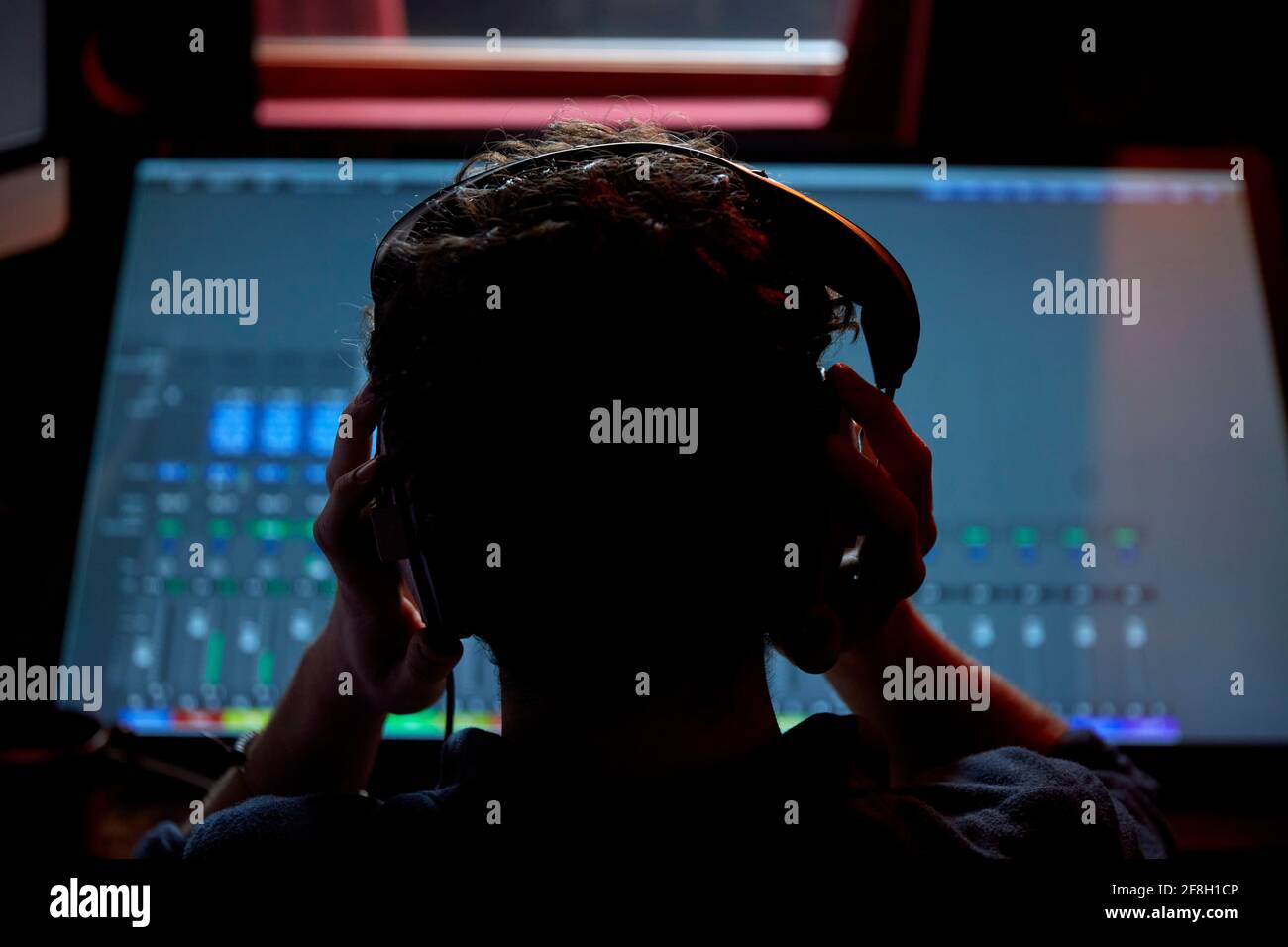 Man working in music studio wearing headphones using large computer screen shot from behind Stock Photo