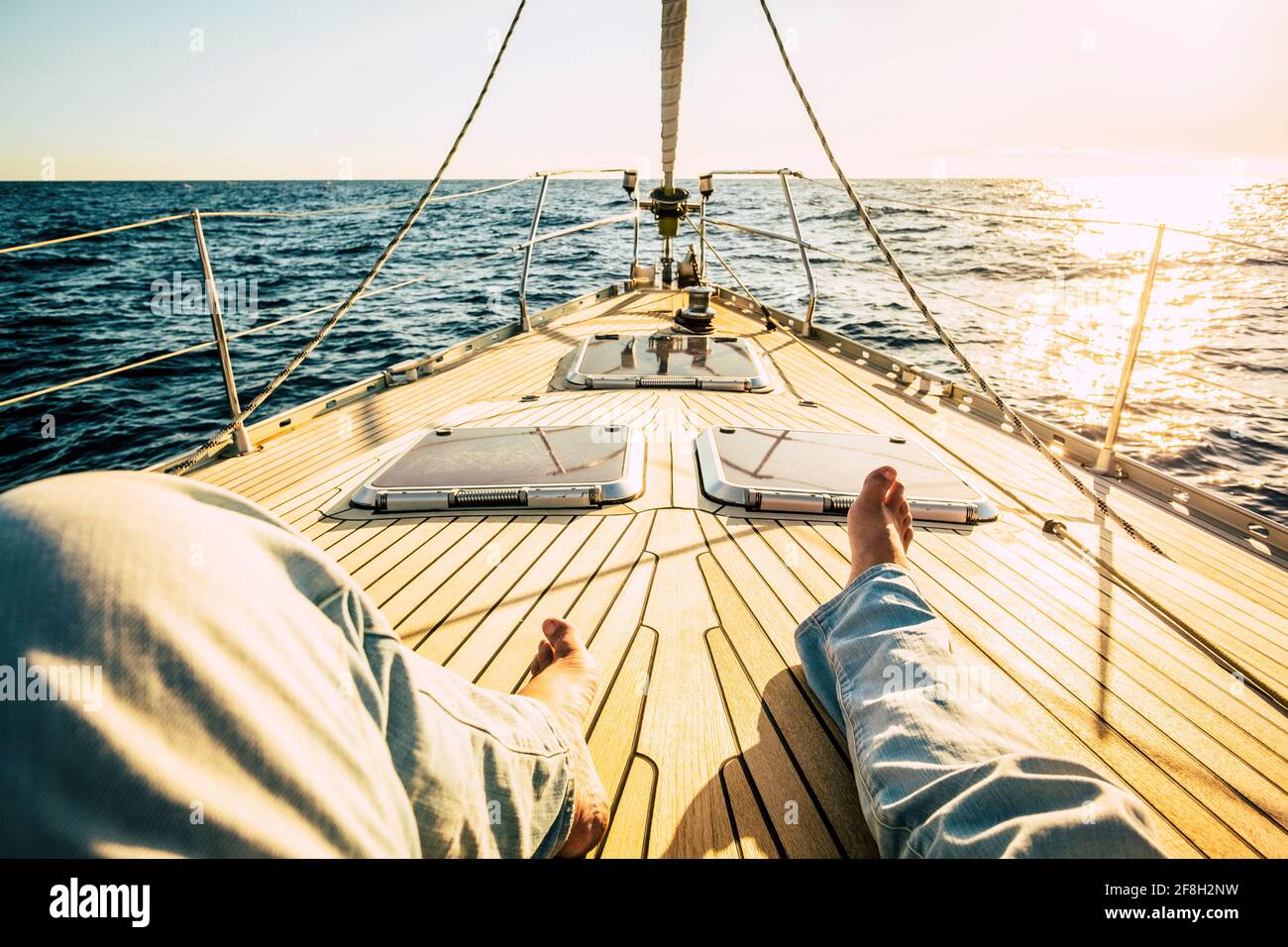 pov point of view of man legs laying and relaxing on the wooden sail boat deck alone with sunset in background - concept of travel people and freedom Stock Photo