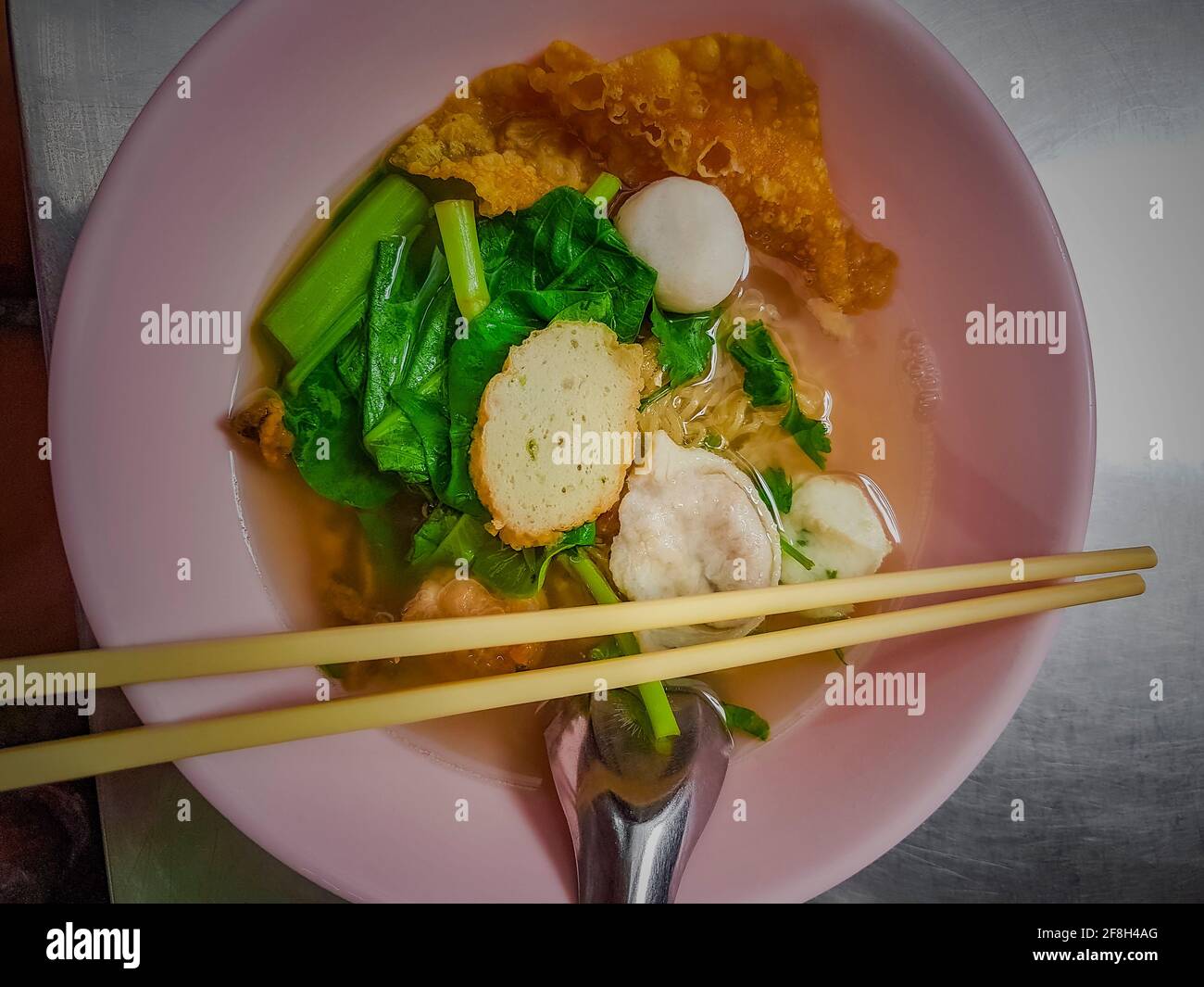 Thai noodle soup with fish balls in pink bowl with chopsticks and spoon