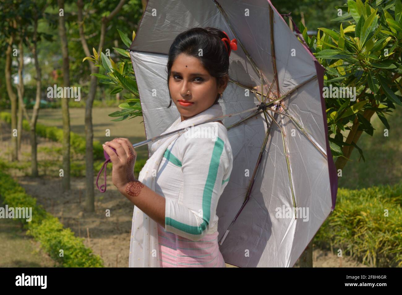 Teenage Indian Bengali girl wearing white cotton salwar holding an umbrella in a village farm, selective focusing Stock Photo