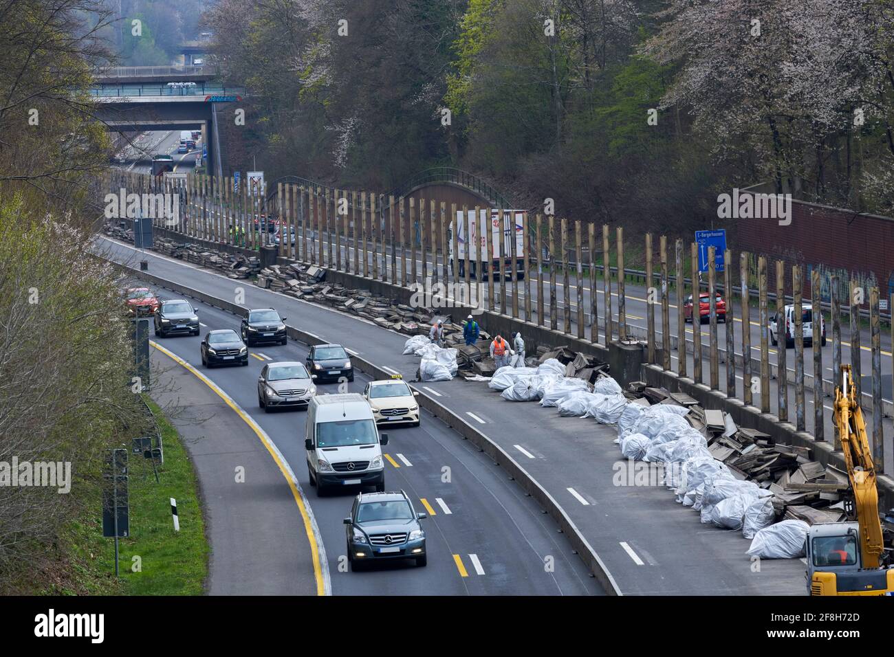 Sanierung Laermschutzwand auf der A52. Mehrere Arbeiter in Schutzanzuegen und Atemmaske verfrachten den Inhalt von Schallschutzelementen in weisse Sae Stock Photo