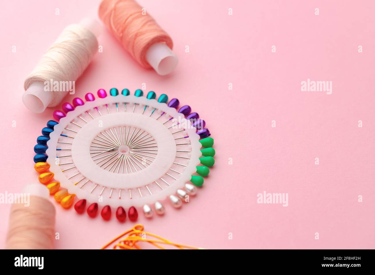 Sewing accessories including thread spools and pins on pink background ...