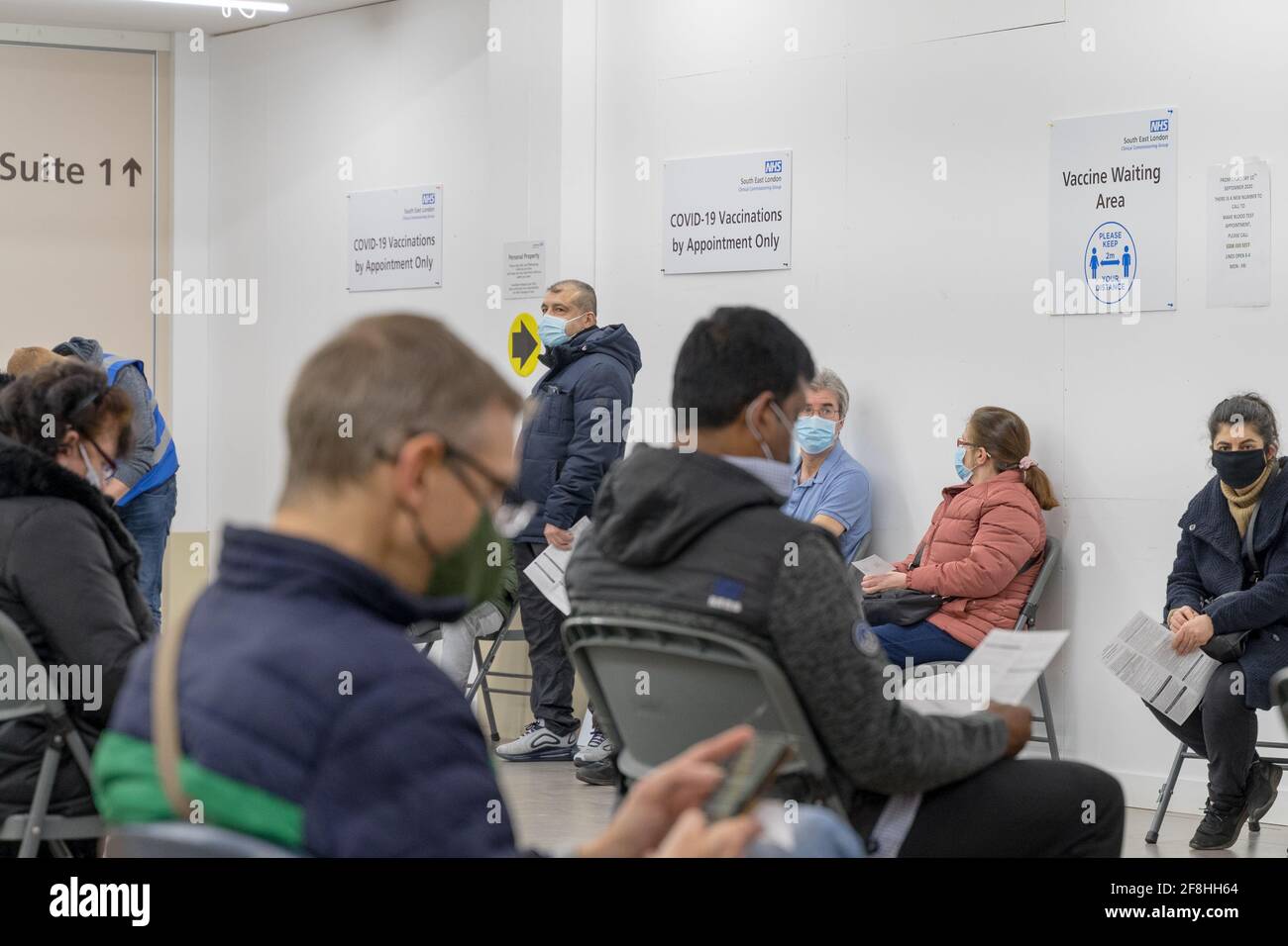 Men and women in face masks with appointments for NHS COVID-19 vaccinations wait in the designated Waiting Area at a clinic in South East London UK Stock Photo