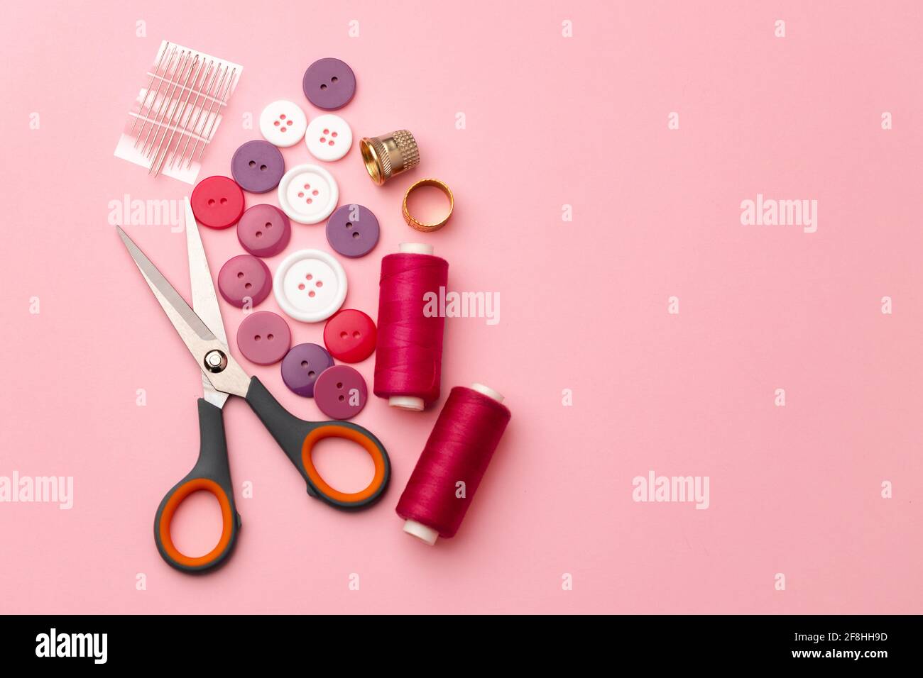Sewing accessories including thread spools and pins on pink background ...
