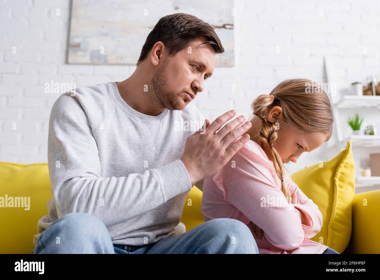 offended girl sitting with crossed arms near discouraged father Stock Photo