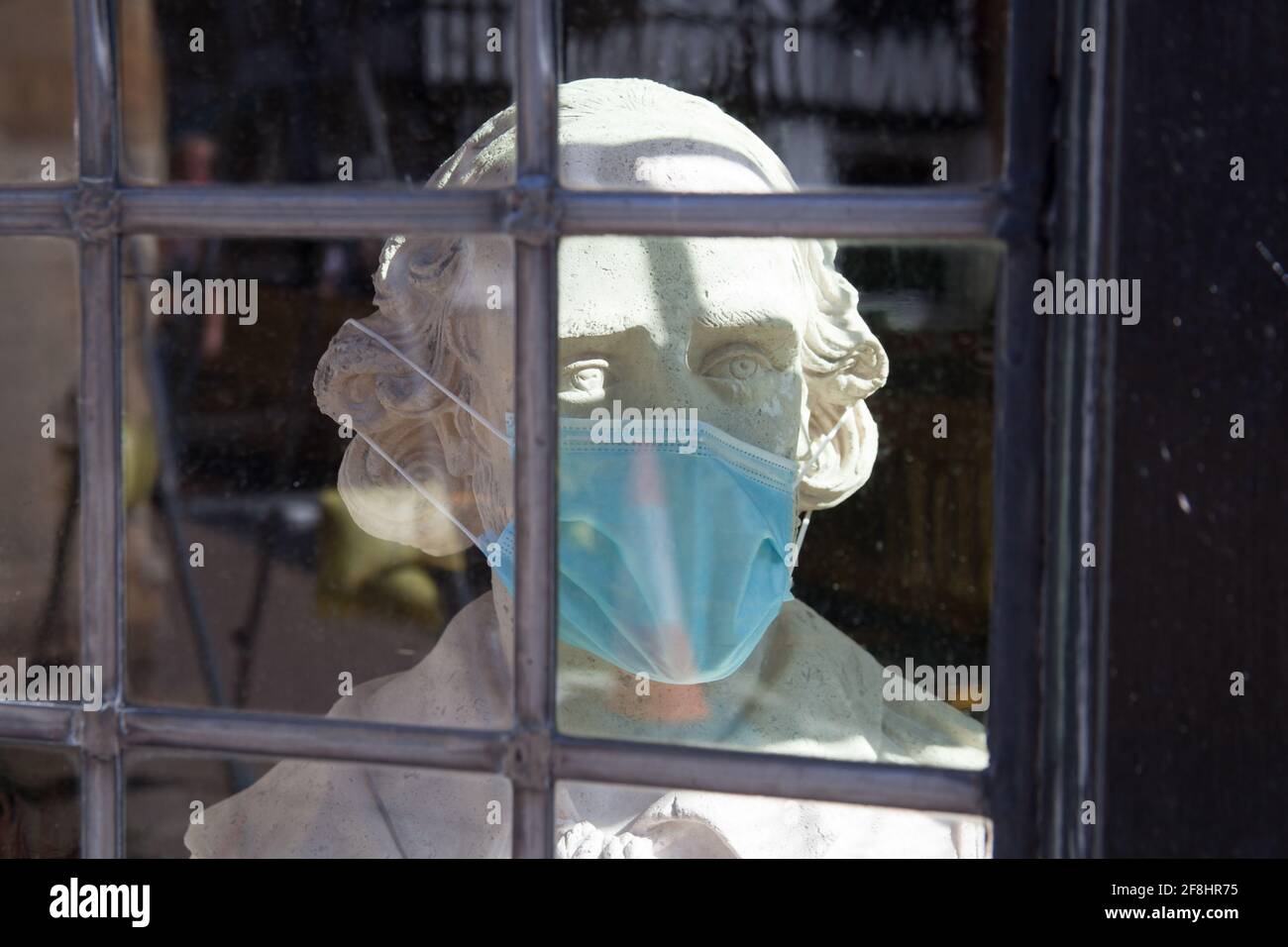 A bust of William Shakespeare with a surgical face mask in a window in Stratford upon Avon in Warwickshire in the UK during the 2020 Covid 19 pandemic Stock Photo