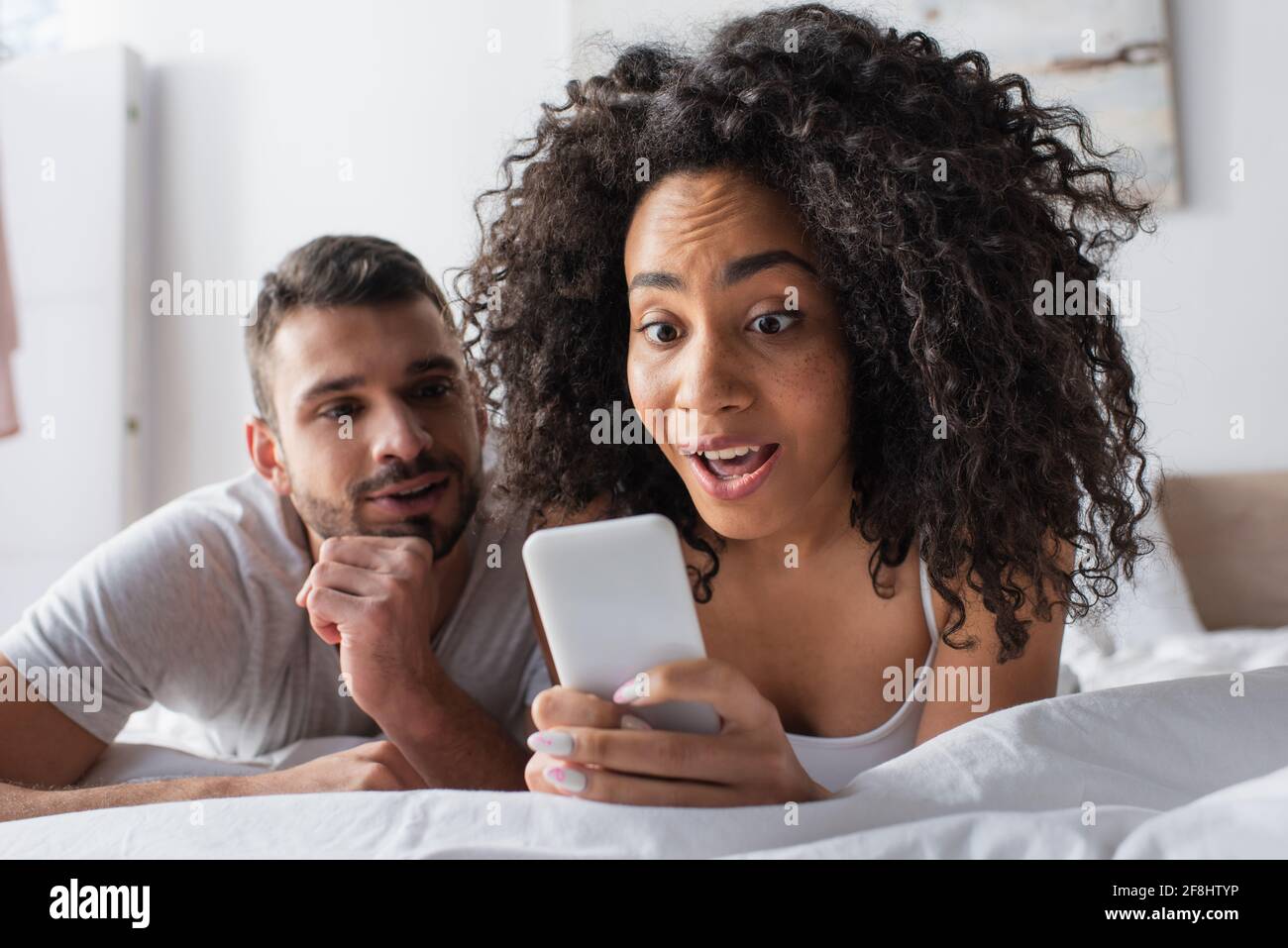 surprised african american woman holding smartphone near bearded boyfriend on blurred background Stock Photo