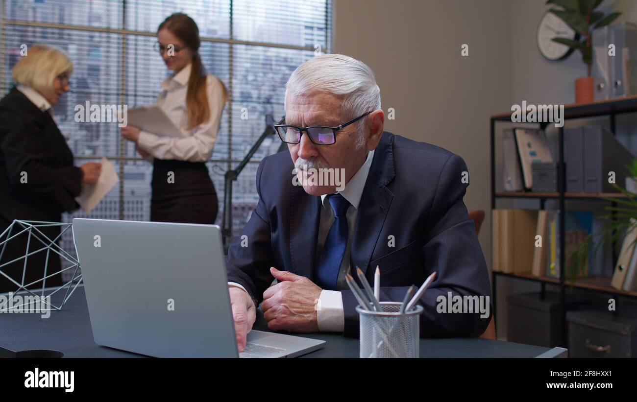 Senior freelancer concentrated developing project while working, typing on laptop computer in office Stock Photo