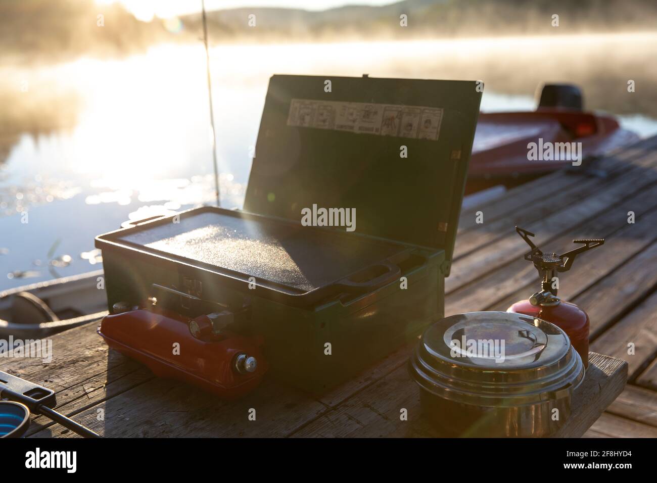 small portable camping stove next to the water at sunrise with a cooking plate on top and a second stove on the side Stock Photo