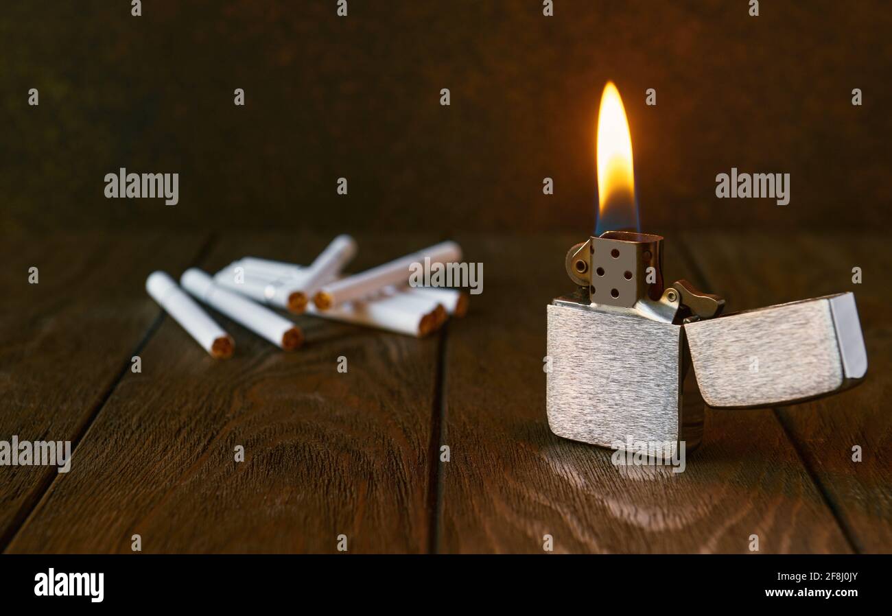 Vintage metal lighter with flame and cigarettes on dark background, close up Stock Photo