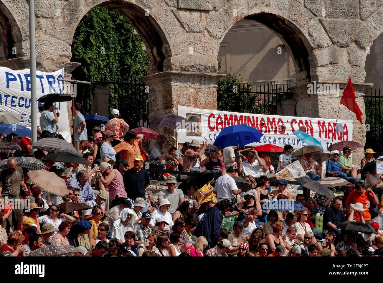 Worshippers at a Roman Catholic music festival and open-air service shelter under sunshades on the stone terraces or cavea of the Pula Arena at Pula, Istria County, Croatia.  The amphitheatre, one of the six largest surviving ancient Roman arenas, was designed to hold up to 23,000 people, but the terraces can now seat only about 7,000.  Pula Arena is now a major music venue and has staged concerts by Foo Fighters, Luciano Pavarotti, Elton John, Sting, Leonard Cohen and David Gilmour. Stock Photo