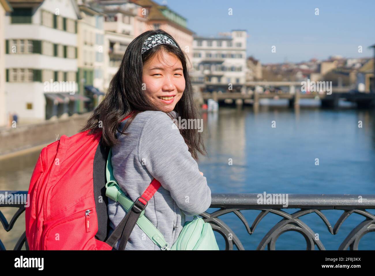 Asian woman backpacker touring in Europe - young happy and pretty Korean girl with backpack having city and river view from bridge during holidays in Stock Photo