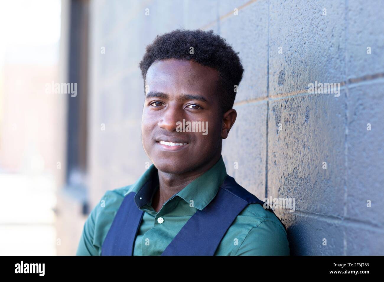 A handsome smiling young black man leans against a gray concrete block wall Stock Photo