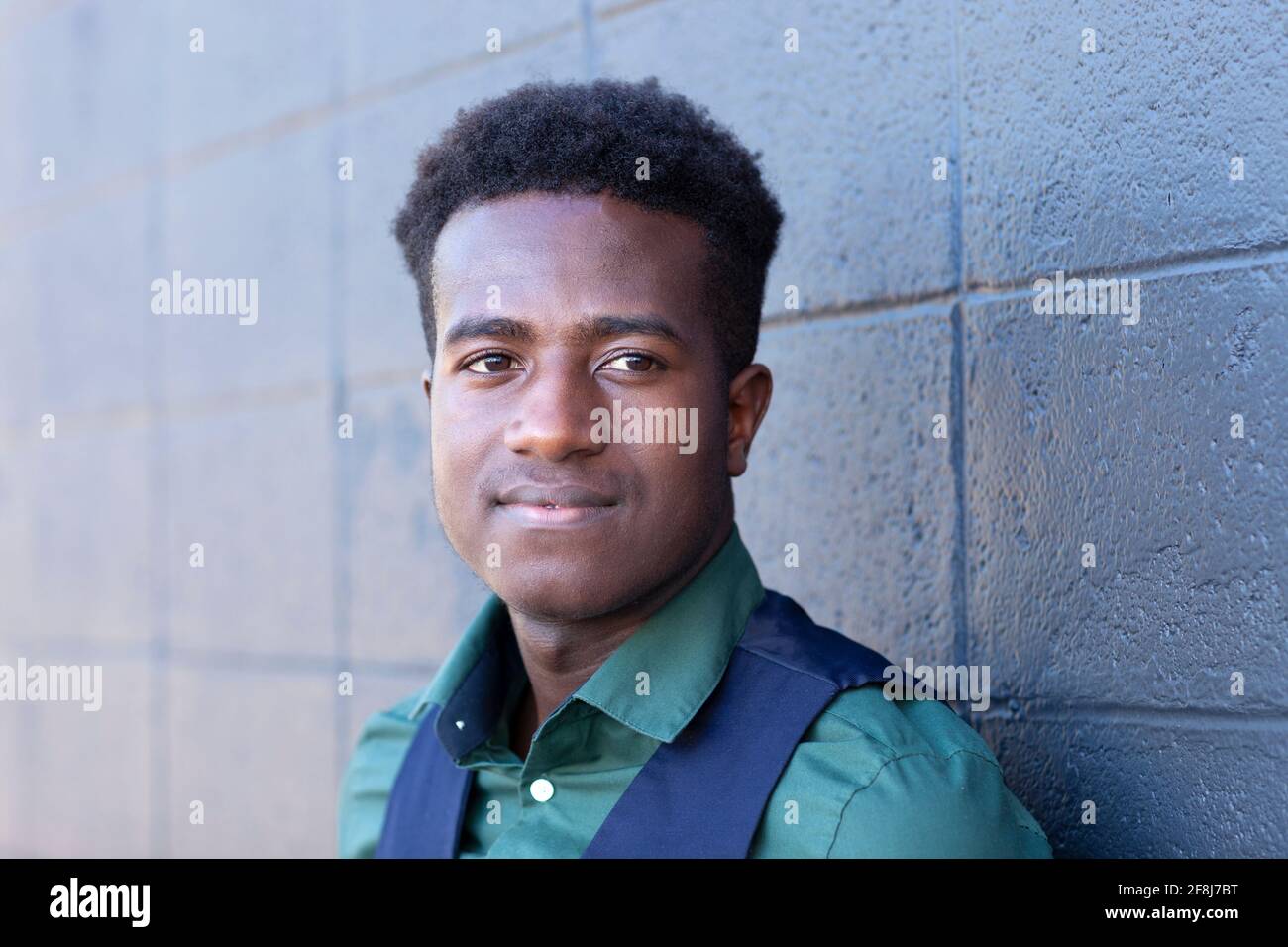 A handsome young black man leans against a gray concrete block wall Stock Photo