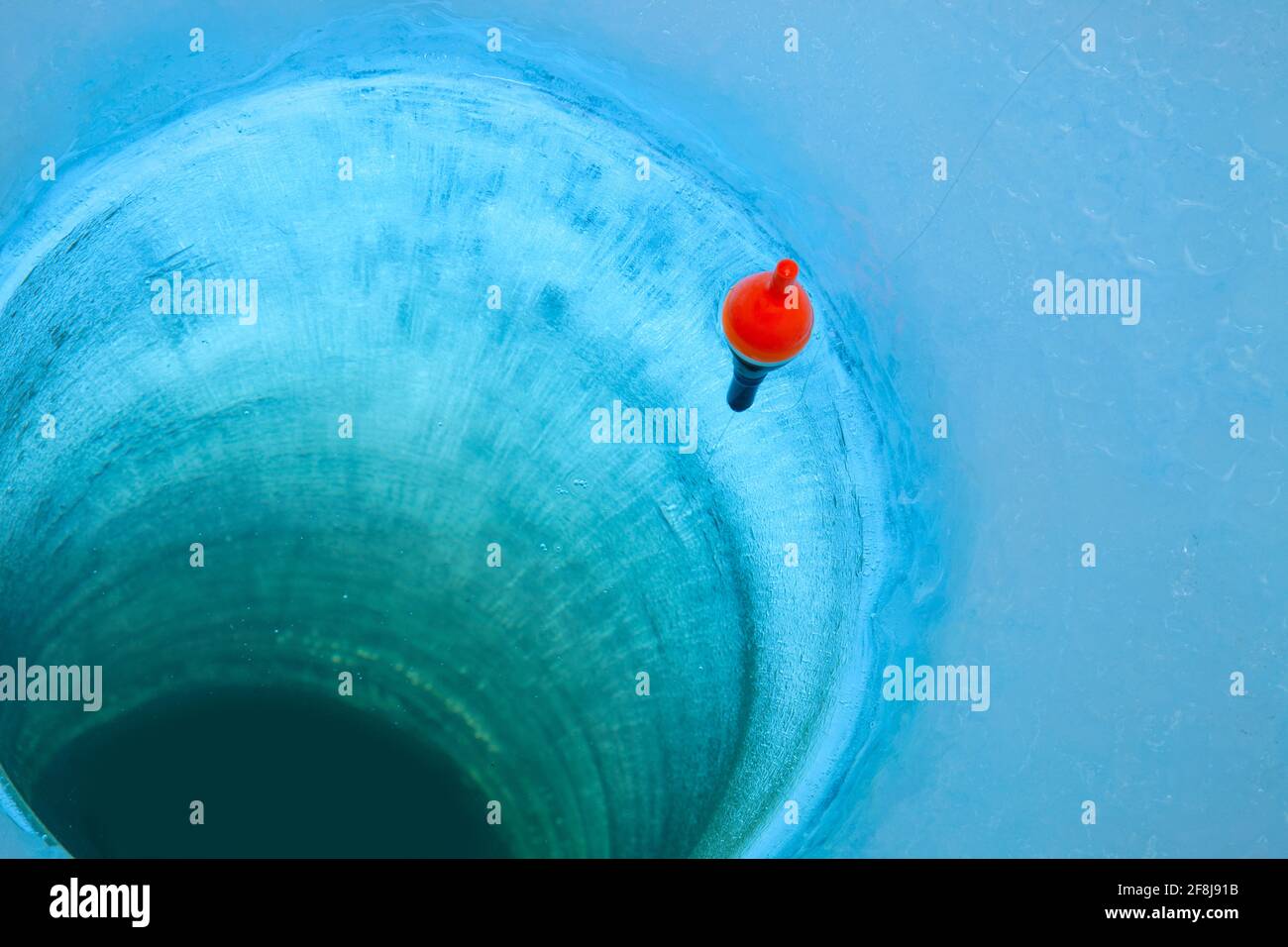 Red bobber and fishing line in an ice fishing hole in a Minnesota lake Stock Photo