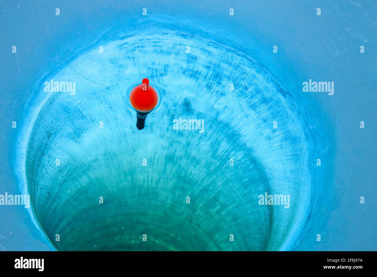 Red bobber and fishing line in an ice fishing hole in a Minnesota lake Stock Photo
