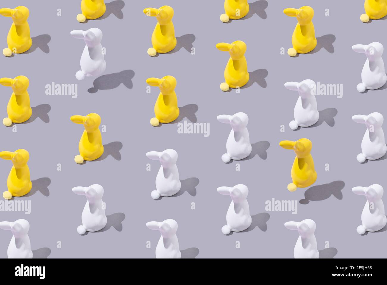 Creative pattern with yellow and white plastic bunny on grey bac Stock Photo