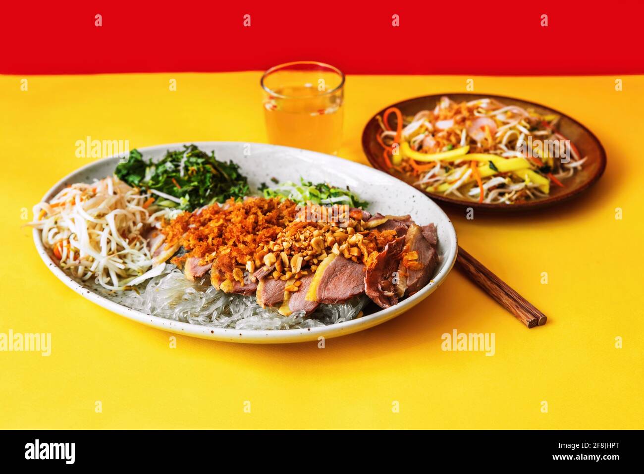 Portion of roasted duck with glass noodle, sprinkled with roasted onion and chopped nuts with herb and vegetable salad, chopstick, glass with vinegar Stock Photo