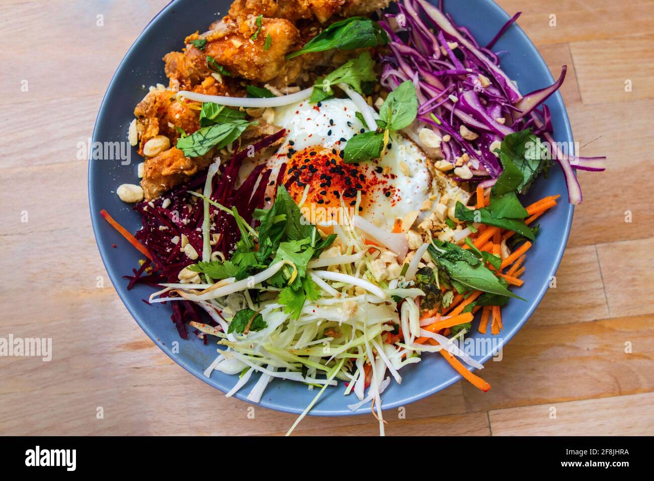 Asian meal with grated raw vegetables (lettuce,cabbage,carrot), green herbs, soft-boiled egg and chicken pieces in breadcrumbs. Stock Photo