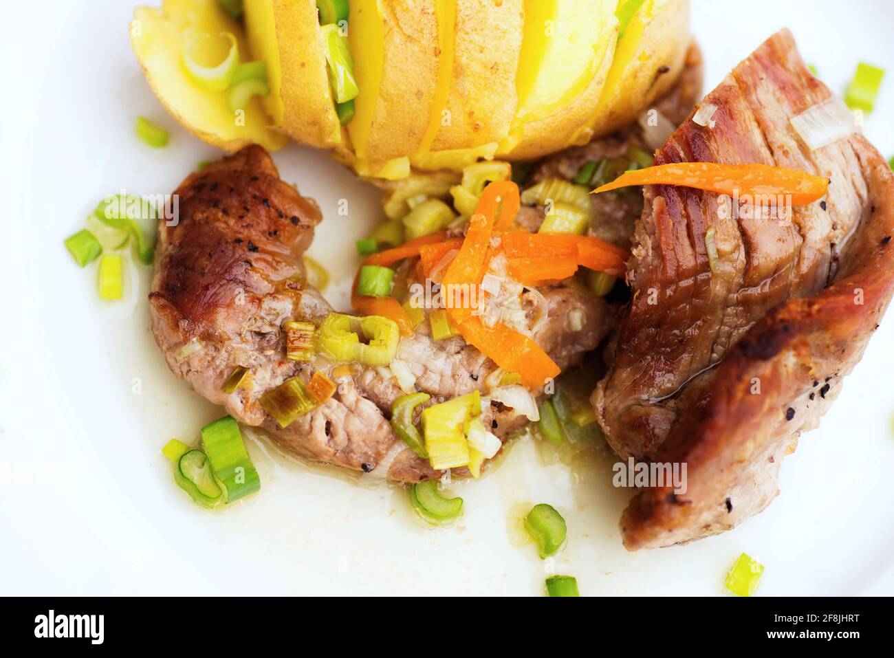 Pork tenderloin with vegetable and boiled cut potato on white plate on light wooden table. Stock Photo