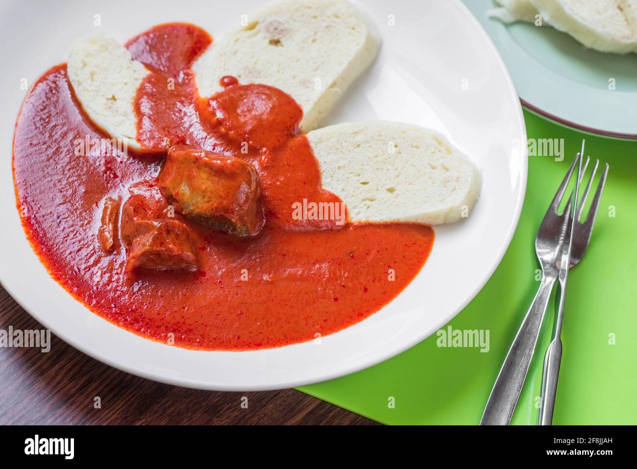 Spicy tomato sauce, beef and dumpling, traditional spicy Czech republic food on white plate, cutlery on table. Stock Photo