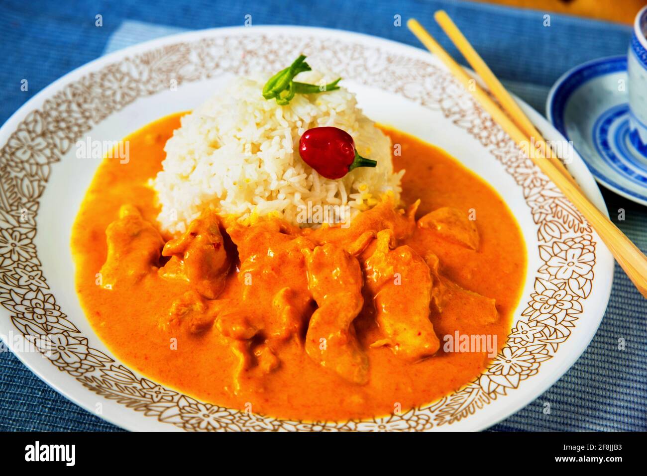 Chicken meat in spicy mango sauce and rice on white plate with chopsticks on blue background, closeup. Asian meal. Stock Photo