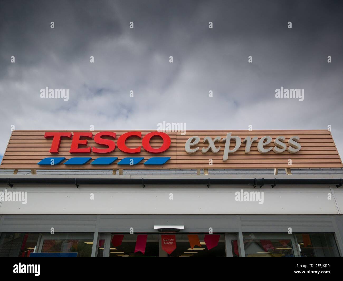 A Tesco Express storefront sign below a dark cloudy sky. Stock Photo